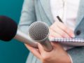 Speaker Holding Two Microphones And Taking Notes For Her Speech.