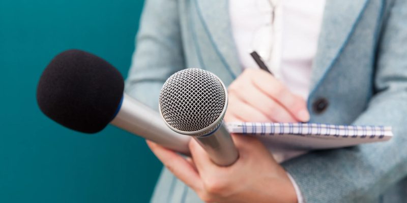 Speaker Holding Two Microphones And Taking Notes For Her Speech.