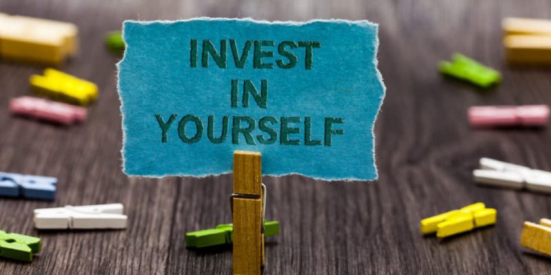 A Text Written Invest In Yourself In A Blue Paper.