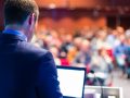 A Blurred Image of A Corporate Meet - A Speaker Speaks Infront of The Audience.